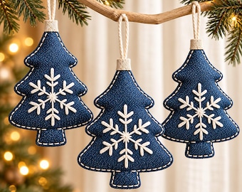 Op de afbeelding: Drie kerstboomhangers van donkerblauwe stof in de vorm van een kerstboom met witte geborduurde sneeuwvlokken. Elke hanger heeft een lichtgekleurd lusje aan de bovenkant en is afgewerkt met witte stiksels langs de randen.