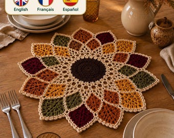 Op de afbeelding: Een ronde gehaakte placemat met een donkerbruin midden, omringd door een bloemmotief van bladeren in tinten bordeauxrood, olijfgroen, mosterdgeel en oranje, allemaal omlijnd met crèmekleurig garen in een ingewikkeld opengewerkt ontwerp.