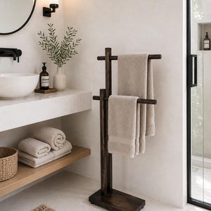 Puede incluir: Un toallero de madera de color marrón oscuro con un poste vertical y una base rectangular. Dos barras horizontales se extienden desde el poste a diferentes alturas, cada una sosteniendo una toalla beige doblada. Estructura de madera.