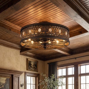 May include: A round flush mount ceiling light fixture featuring a dark bronze metal frame with intricate scrollwork patterns and embedded clear crystal accents. The drum-shaped design includes a spoked metal base and multiple internal light bulbs.