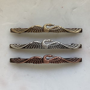 K&ouml;nnte beinhalten: Drei dekorative Haarklammern aus Metall in Form eines Schwans in Gold-, Silber- und Kupferausf&uuml;hrung. Jede Klammer zeigt ein detailliertes Schwanendesign mit ausgebreiteten Fl&uuml;geln.