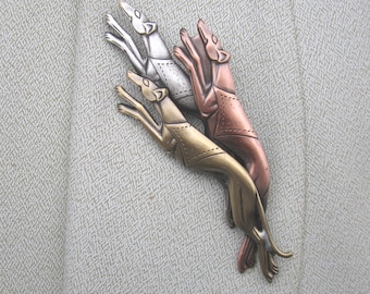 Pode incluir: Um broche de prata, ouro e cobre com três galgos estilizados saltando no ar.
