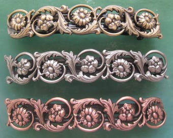 May include: Three ornate hair clips with floral designs. The clips are made of metal and are available in gold, silver, and copper.