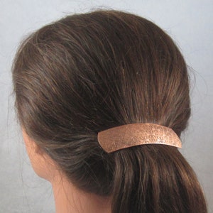 Puede incluir: Una pinza para el pelo de cobre con un dise&ntilde;o floral. La pinza mide aproximadamente 5 cm de largo y se muestra puesta en una coleta.