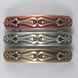 K&ouml;nnte beinhalten: Drei verzierte Haarklammern in verschiedenen Ausf&uuml;hrungen: Kupfer, Silber und Gold. Jede Klammer hat ein dekoratives, symmetrisches Design mit einer zentralen ovalen Form und filigranen Schn&ouml;rkeln.