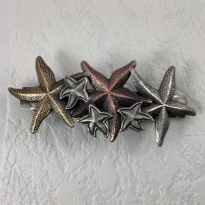 May include: A cluster of five metal starfish hair clips in silver, copper, and gold tones. The starfish are arranged in a cascading pattern.