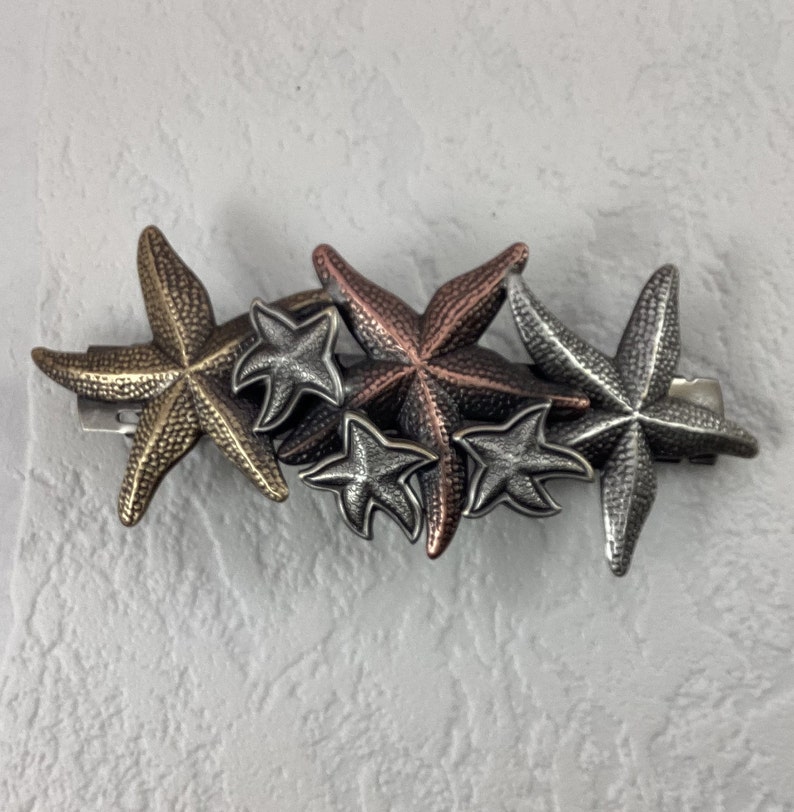 May include: A cluster of five metal starfish hair clips in silver, copper, and gold tones. The starfish are arranged in a cascading pattern.