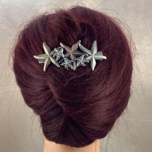 Può includere: Un fermaglio per capelli argentato con cinque ciondoli a forma di stella marina. Le stelle marine sono in diverse tonalità di argento, oro e rame.
