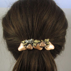 Puede incluir: Una pinza para el pelo de cobre y plata con un dise&ntilde;o de tres fresas y hojas.