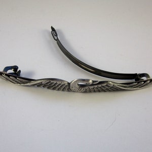 K&ouml;nnte beinhalten: Silberne Schwanen-Haarklammer mit schwarzem Metallstab. Der Schwan hat ausgebreitete Fl&uuml;gel und ein detailliertes Design.