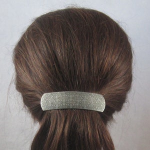 Puede incluir: Una pinza para el pelo de plata con un patr&oacute;n floral. La pinza tiene forma de rect&aacute;ngulo y se utiliza para sujetar una coleta.