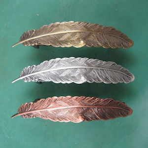 May include: Three feather-shaped hair clips in gold, silver, and copper.