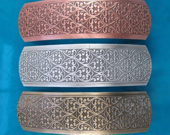 May include: Three decorative hair clips with an ornate floral design. The clips are made of metal and are available in copper, silver, and gold.