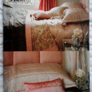 May include: Simplicity 4600 bedding pattern. The image shows a bed with a peach-colored comforter and pillows. A decorative pillow with button accents is in the foreground. The bedding has a luxurious, silky appearance.