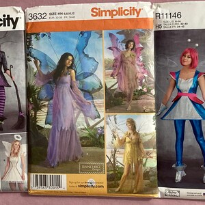 May include: Three Simplicity sewing pattern envelopes featuring costume designs. The patterns depict various costumes, including a fairy, witch, angel, and futuristic space-themed outfits. The envelopes are in shades of purple, blue, and red.
