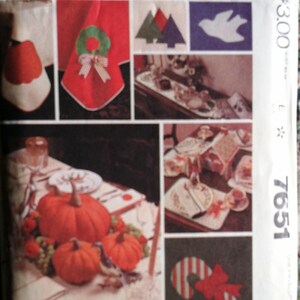 May include: McCall's sewing pattern envelope featuring various holiday-themed designs. Includes images of a red napkin with a green wreath, pumpkins, and a candy cane with a red bow. The pattern number is 7651.