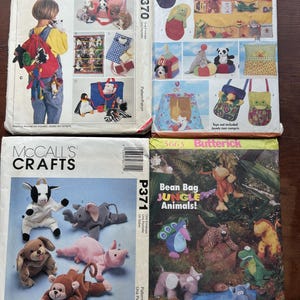 May include: Four vintage sewing pattern envelopes. Two McCall's Crafts patterns feature stuffed animal designs, including a backpack and various plush toys. Two Butterick patterns showcase bean bag jungle animals and other soft toy designs.