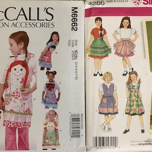 May include: Two vintage sewing pattern envelopes. The McCall's envelope features children wearing aprons with doll faces. The Simplicity envelope shows various apron and dress designs for kids. Both patterns are for sizes 3-8.
