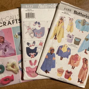 May include: Three sewing patterns for children's clothing. The patterns are from McCall's Crafts and Butterick. The patterns include a hooded robe, a hooded towel, and a bib. The patterns are all in one size.