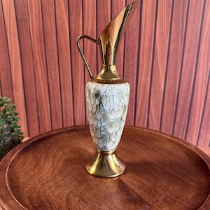 May include: A decorative pitcher featuring a polished gold-tone metal neck, handle, and base. The central body is crafted from white ceramic with a textured, crackled surface pattern in shades of green, creating a distinct visual contrast.