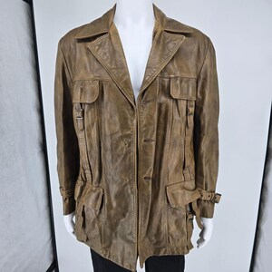 May include: A brown leather jacket featuring a collared neckline, a button-front closure, and multiple utility-style pockets on the chest and waist. The jacket includes adjustable buckle straps on the sides and cuffs, with a weathered, textured finish.