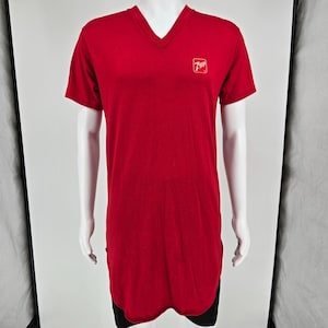 Peut inclure: Un t-shirt rouge vif à manches courtes avec une encolure en V. Le vêtement présente un petit logo 7UP blanc imprimé sur la poitrine supérieure gauche. Il possède un ourlet long et incurvé qui descend sous la taille, créant une silhouette allongée.