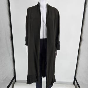 May include: A long, open-front black duster coat featuring long sleeves with pleated cuffs and a matching pleated hemline. The garment has a smooth, lightweight texture and falls to a mid-calf length, providing a layered look over dark pants.