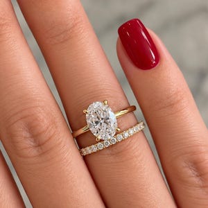May include: A gold ring set featuring an oval-cut centre stone held by four prongs on a plain band, paired with a matching eternity band encrusted with small round stones. Both rings are crafted from polished yellow gold metal.