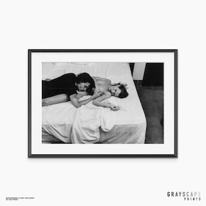 Könnte beinhalten: Ein schwarz-weiß gerahmter Kunstdruck, der zwei Personen zeigt, die zusammen auf einem Bett mit weißer Bettwäsche liegen. Der Druck ist in einem dünnen schwarzen Rahmen mit weißem Passepartout gefasst. Der Text GRAYSCAPE PRINTS steht unten rechts.