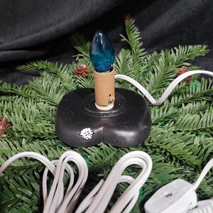 Puede incluir: Una bombilla azul sobre una base negra con un cable blanco. El cable est&aacute; enrollado y tiene un enchufe en el extremo.