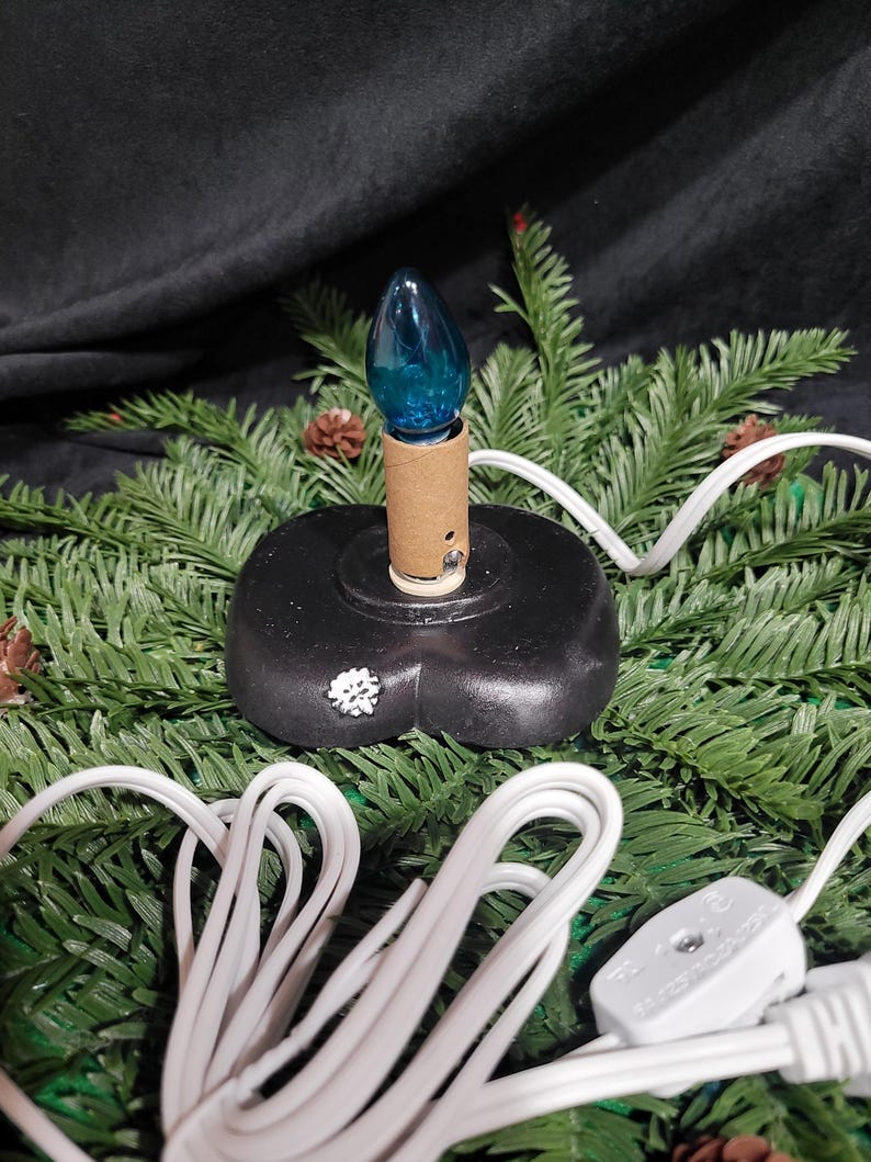 Puede incluir: Una bombilla azul sobre una base negra con un cable blanco. El cable est&aacute; enrollado y tiene un enchufe en el extremo.