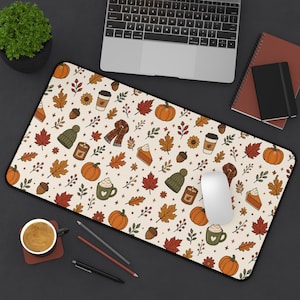 May include: A rectangular desk mat featuring a repeating autumn-themed pattern on a cream background. The design includes orange pumpkins, brown acorns, red and orange maple leaves, green knit hats, plaid scarves, candles, and mugs of coffee.