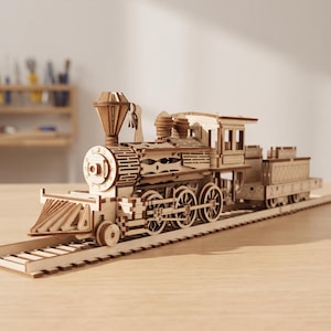 May include: A light brown wooden model steam locomotive train with a detailed boiler, a tall smokestack, and a cowcatcher at the front. The train is positioned on a matching wooden track, featuring intricate laser-cut patterns and visible gear components.