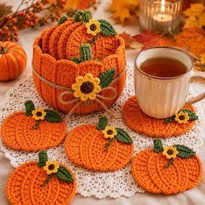 Puede incluir: Un juego de posavasos de ganchillo con forma de calabaza naranja, con tallos verdes y detalles de girasoles amarillos, guardados en una cesta de ganchillo a juego. La cesta está atada con cuerda y decorada con un girasol.