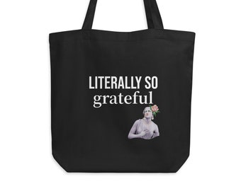 Könnte beinhalten: Schwarze Tragetasche mit weißem Text "LITERALLY SO grateful". Unter dem Text befindet sich eine Grafik einer Statue mit einer Blume. Die Tasche hat zwei schwarze Griffe und hängt an einem schwarzen Haken.