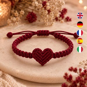 Puede incluir: Una pulsera de macramé de color rojo oscuro con un diseño central de nudo en forma de corazón. La pulsera está construida con cordón y un mecanismo de cierre de nudo deslizante, lo que permite ajustar el tamaño. El cordón está trenzado.