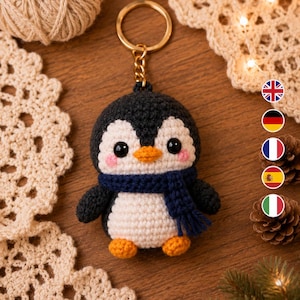 Könnte beinhalten: Ein gehäkelter Pinguin-Schlüsselanhänger mit schwarz-weißem Körper, kleinem orangefarbenem Schnabel, orangefarbenen Füßen und einem dunkelblauen Schal. Der Pinguin hat schwarze Perlenaugen und rosa gestickte Wangen an einem goldenen Ring.