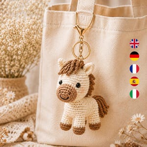 Peut inclure: Un porte-clés cheval crocheté crème et marron avec un fermoir et un anneau en métal doré. Le cheval présente une crinière texturée, un museau marron foncé et des sabots marron foncé, attaché à un sac fourre-tout en toile beige clair.