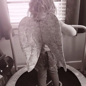 May include: A child wearing angel wings, standing on a small trampoline. The wings are a light grey with a star pattern. The child is wearing a skirt with star patterns and leggings. The trampoline has the word "Fun" on it.