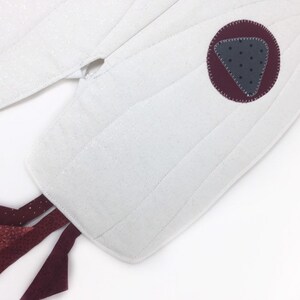 May include: White quilted oven mitt with a claret circle and a grey triangle with black dots. The mitt has a tail of claret fabric with white dots and geometric shapes. The mitt is on a white background.