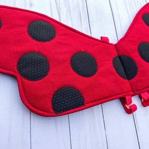 Op de afbeelding: Rode lieveheersbeestvleugels met zwarte stippen. De vleugels zijn gemaakt van vilt en hebben een zachte textuur. De vleugels zijn aan elkaar bevestigd met een stuk stof.