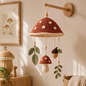 May include: A crochet mobile featuring a large rust-colored mushroom cap with white spots, suspended from a wooden wall mount. Hanging from the cap are smaller crochet elements including a mushroom, an acorn, and green leaves on strings.