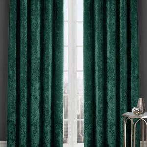 May include: A pair of floor-length, deep emerald green crushed velvet curtains featuring silver metal grommets at the top. The curtains hang from a silver rod, displaying a textured, light-reflecting fabric surface with vertical folds.