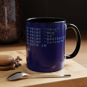 May include: A dark blue ceramic mug with a black handle and interior, featuring white computer code text that reads: 10 PRINT "This", 20 PRINT "Mug", 30 PRINT "Is", 40 PRINT "BASICally", 50 PRINT "Infinite", 60 GOTO 10, and the word RUN at the bottom.