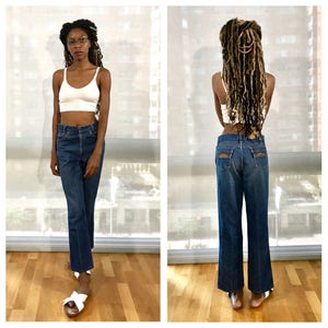 Pode incluir: Uma pessoa vestindo um top branco curto e jeans azul denim de perna larga. O jeans tem cintura alta e um caimento relaxado.
