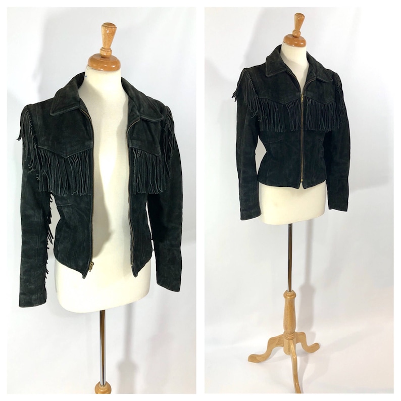 May include: A black suede jacket with fringe detailing on the shoulders and sleeves. The jacket has a zipper closure and a fitted silhouette.