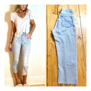 May include: Light blue denim jeans with a high waist and a straight leg. The jeans have a frayed hem and are slightly distressed.