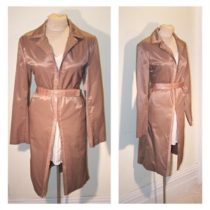 May include: A long, brown satin trench coat with a belt and a single-breasted closure. The coat has a slightly flared silhouette and a collar.