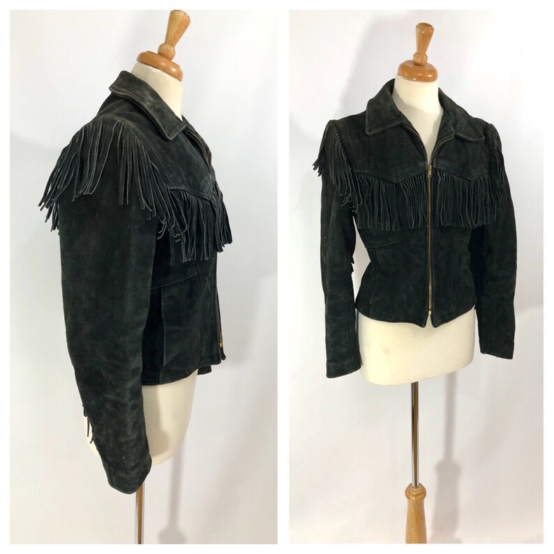 May include: A black suede jacket with fringe detailing on the shoulders, collar, and hem. The jacket has a zipper closure and a fitted silhouette.