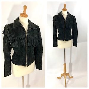 May include: A black suede jacket with fringe detailing on the shoulders and front. The jacket has a zipper closure and long sleeves.